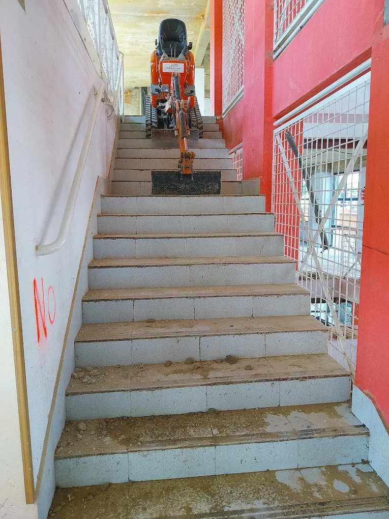 Mini excavadora bajando por una escalera en una obra